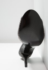 Talons aiguilles noirs avec un bout effilé et élégant, orné d'accents métalliques et de motifs texturés le long des bords. Fini lisse et brillant.