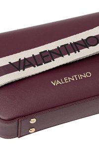 Borsa Valentino in pelle bordeaux, con finitura testurizzata, accessori in oro e una tracolla in tessuto a strisce con scritte nere.