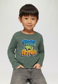 Groene long-sleeve t-shirt met de graphic "TIME TO ACT" in blauw, groen en oranje, gecombineerd met grijze textuur jeans.