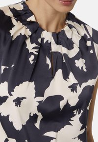 Navy floral blouse featuring a pleated neckline with a keyhole detail, made of smooth fabric with a cream floral pattern.