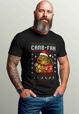 Black T-shirt featuring a colorful graphic of a fish in a Santa hat holding cookies, with holiday-themed patterns and text "CARB-FAN."