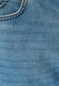 Tessuto di denim blu chiaro con una sottile texture, caratterizzato da una cucitura e dettagli di cucitura visibili in un colore marrone a contrasto.