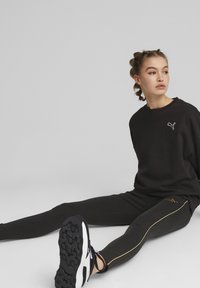Musta sweatshird valge logoga, mustad retuusid kuldse külgtriibuga, koos mustade ja valgete spordijalatsitega. Sujuv tekstuur, mugav lõige.