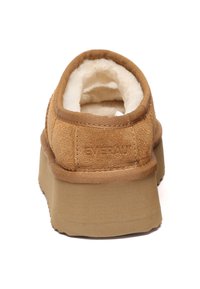 Brown suede slip-on shoe with a fluffy beige lining, featuring a thick, textured sole and subtle branding on the back.