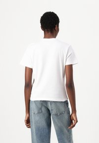 Witte katoenen T-shirt met een ronde hals en korte mouwen, met een relaxed fit. G gedragen met lichtblauwe denim jeans.