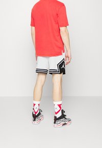 Person wearing white and black basketball shorts, red and white Jordan socks, black and white patterned sneakers, and a red t-shirt, standing.