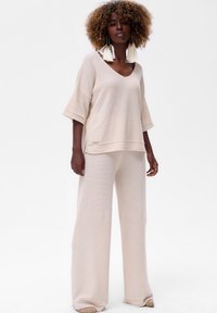 Top en tricot beige avec un col en V et des manches larges, associé à un pantalon large assorti. Tissu texturé avec un motif subtil.