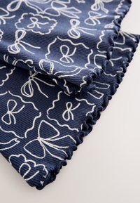 Tessuto blu navy con motivo a fiocco bianco, caratterizzato da una texture a coste e bordi smerlati. Il design è morbido e flessibile.