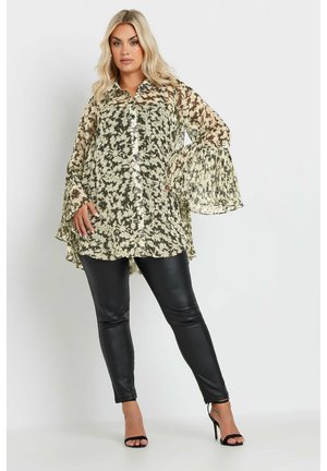 Doorzichtige blouse met een bloemenpatroon in tinten groen en crème; heeft bell sleeves en een knoopsluiting aan de voorkant. Gecombineerd met zwarte leren pantalons.