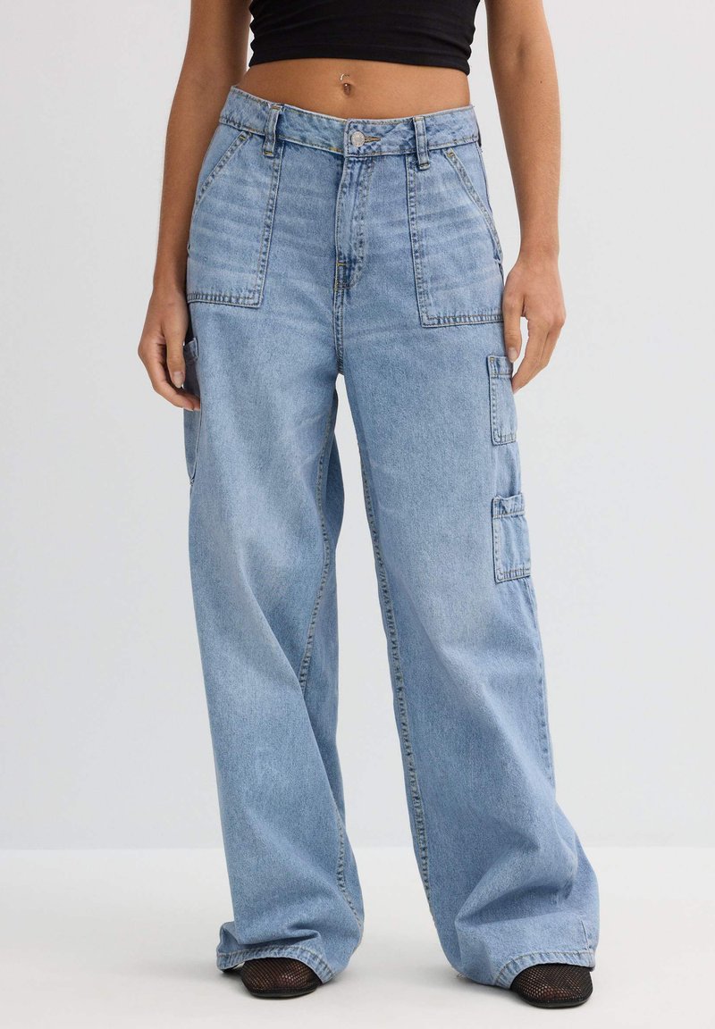 Pantalones cargo de mezclilla azul claro con un corte relajado, que cuentan con dos bolsillos frontales y un bolsillo lateral, destacando costuras en contraste y un cierre de botón.