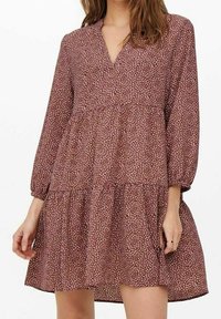 Variación de un vestido burdeos oscuro con mangas largas, escote en V y un dobladillo en capas. Presenta un pequeño patrón blanco parecido a hojas en toda la prenda.