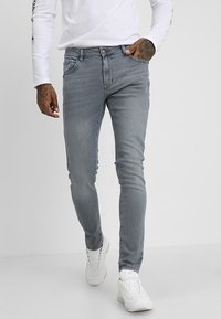 Jeans ajustados de color gris claro con diseño de cinco bolsillos, ligero desvanecimiento y una cómoda tela elástica, combinados con una camisa blanca de manga larga lisa.