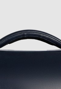 Marineblauwe leren tas met een gladde textuur, voorzien van een gebogen handvat bekleed met zwarte stof en zichtbare stikdetails.