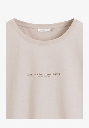 Beżowa koszulka z okrągłym dekoltem z nadrukiem "LIFE IS ABOUT CHALLENGES ATLANTIC SINCE 1994" wypisanym wielkimi literami na środku przodu.