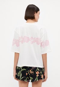 Witte T-shirt met korte mouwen, voorzien van een roze bloemenprint op de rug. Gepaard met zwarte bloemenshorts. Ontspannen pasvorm, zachte textuur.