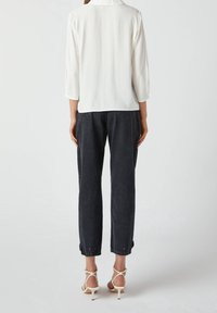 Biała bluzka z długim rękawem i złożonym kołnierzykiem, zestawiona z ciemnoniebieskimi dżinsami. Dżinsy mają luźny krój i podwinięte mankiety. Białe sandały na obcasie.