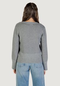 Maglione grigio in maglia con maniche lunghe, polsini e orlo a coste, con una texture liscia. Abbinato a jeans in denim azzurro chiaro.