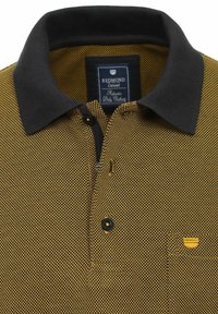 Koszulka polo z czarnym kołnierzykiem, w żółto-czarne kratki, z jednym guzikiem i małym żółtym haftem na piersi.