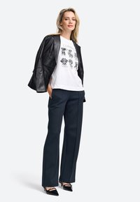 Black leather jacket, white graphic t-shirt with illustrations, navy trousers, and black pointed heels. Modern casual outfit.