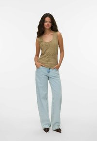Top senza maniche color verde oliva con scollatura rotonda e una leggera texture, abbinato a jeans in denim a gamba larga di colore blu chiaro e scarpe scure a punta.