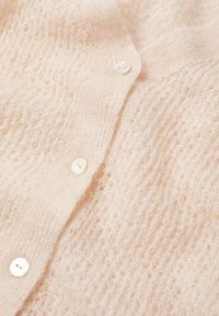 Hellrosa Cardigan aus flauschigem Material mit weicher Textur, ausgestattet mit vier weißen Knöpfen und einem strukturierten Muster.