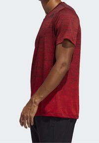 Camiseta atlética roja de manga corta con un patrón texturizado y un acento del logo negro en el hombro. Diseño ligero con cuello redondo.