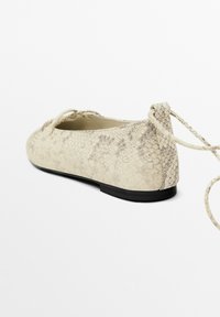 Ballerine con un'esterno beige a motivo serpente, lacci sottili, punta tonda e suola nera, caratterizzate da una texture liscia.