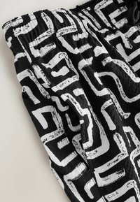 Pantalones cortos de tela en blanco y negro con un audaz patrón abstracto. El material es ligero y cuenta con una cinturilla elástica y cordón.