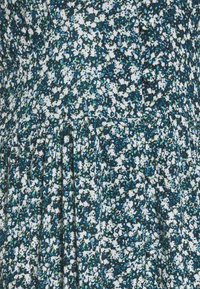 Vestido de estampado floral que presenta una mezcla de colores azul, verde y blanco, con una tela texturizada, falda plisada y botones en la parte delantera.