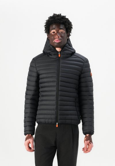 Doudoune noire avec un design matelassé, fermeture éclair et capuche. Elle possède des poignets élastiques et un accent orange sur la fermeture éclair.
