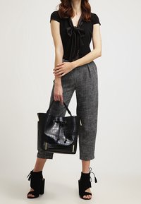 Svart fluga-blus, grå rutiga skräddarsydda byxor och svarta sandaler med blockklack. Svart handväska med krokodilmönster och dragsnöre.