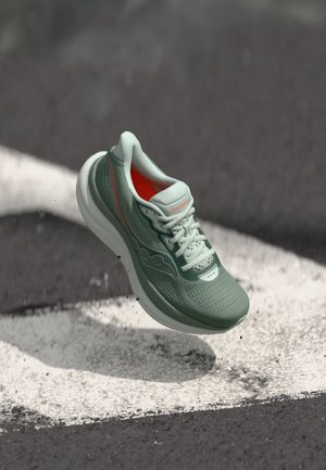 Baskets de course vert clair avec un dessus en maille texturée, semelle blanche et accents orange. Présente des lacets et des perforations pour la respirabilité.