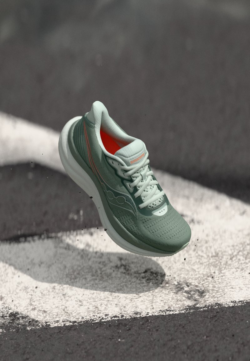 Zapatilla de correr verde claro con parte superior de malla texturizada, suela blanca y detalles en naranja. Presenta cordones y perforaciones para mayor transpirabilidad.