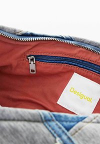 Vista interna di una borsa in denim con fodera rossa, una tasca interna con zip e un'etichetta bianca con testo giallo "Desigual".