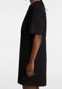 Czarna oversize sukienka t-shirtowa wykonana z bawełny, z krótkimi rękawami, okrągłym dekoltem i małą metką z logo na dole.