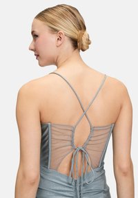 Robe bleue scintillante avec fines bretelles, dos ouvert avec détails en mesh, fermeture nouée et tissu texturé.