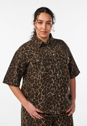 Žena s tmavými kučeravými vlasmi má na sebe krátku rukáv, košeľu na gombíky a zodpovedajúce nohavice s hnedo-čiernym zvieracím vzorom.