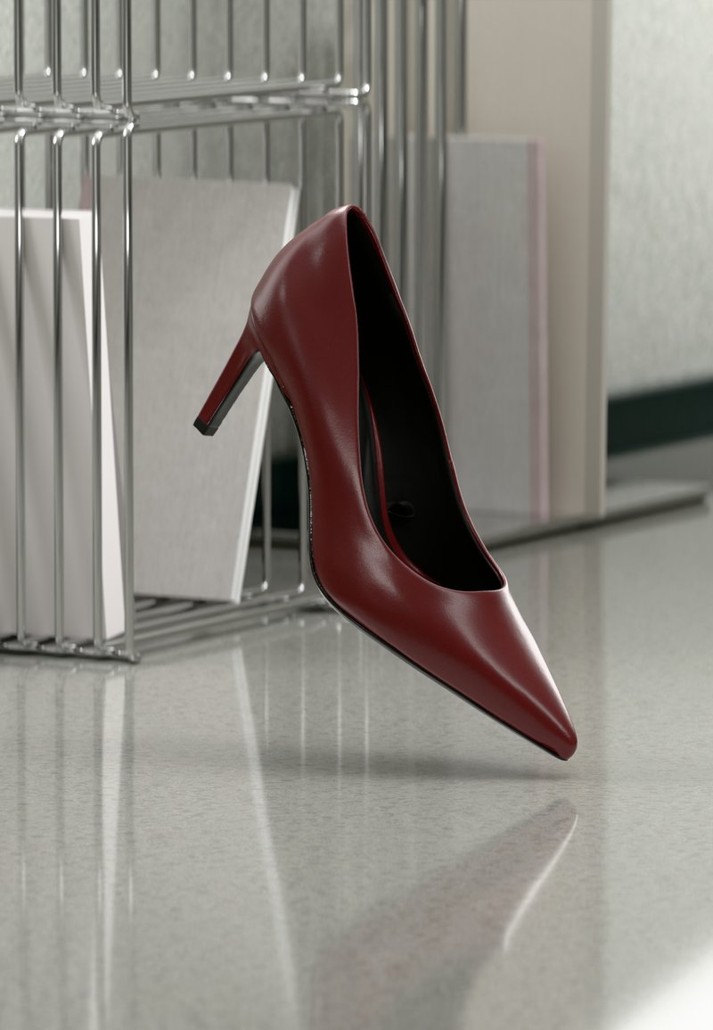 Μονό σκουρό κόκκινο ψηλοτάκουνο παπούτσι με μυτερή μύτη τοποθετημένο σε αντανακλαστικό δάπεδο ανοιχτού χρώματος κοντά σε μεταλλικό οργανωτή αρχείων.