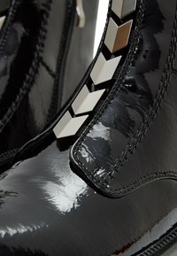 Botas de charol negras con un diseño elegante, superficie texturizada y un patrón geométrico en contraste a lo largo del costado.