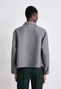 Casaco cinza em mistura de lã com gola, design cropped e punhos com botão. Apresenta um rótulo subtil perto da gola.