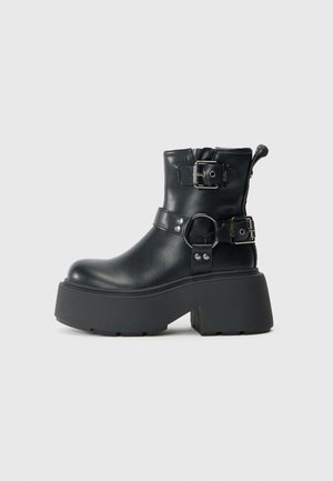 Black leather ankle boot with a rounded toe, chunky platform sole, adjustable buckle straps, and a textured rubber tread.