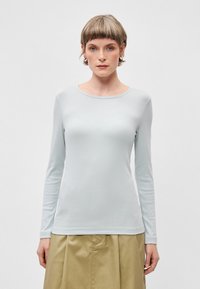 Top de manga longa azul claro em tecido canelado com decote redondo, combinado com uma saia drapeada bege. Design simples e ajustado.