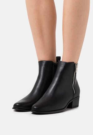 Botines de cuero negro con punta puntiaguda, cierre lateral con cremallera y tacón bajo de bloque. Textura lisa y diseño minimalista.