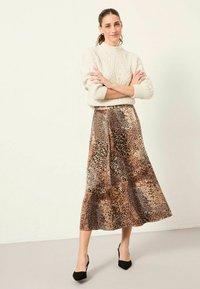 Maxikleid im Leopardenmuster in Beige- und Brauntönen, fließendes Design, satinartige Textur, kombiniert mit einem cremefarbenen Strickpullover und schwarzen High Heels.