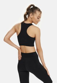 Schwarzer Sport-BH mit Racerback-Design, aus einem strukturierten Stoff und mit einem cropped Schnitt. Kombiniert mit hochtaillierten schwarzen Leggings.