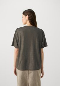 Chemise à manches courtes gris foncé avec un design perforé, col rond et coupe décontractée, associée à une jupe beige clair.