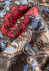 Vuna tkanina s cvjetnim uzorkom u crvenim, plavim i smeđim nijansama. Meka tekstura koja prikazuje složene dizajne i tople boje.