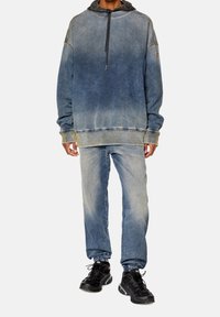 Felpa in denim con gradiente di colore blu, cappuccio con cordino, polsini a coste, abbinata a jeans blu e scarpe da atletica nere.