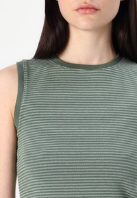 Haut sans manches vert côtelé avec un col rond, présentant un tissu texturé et un motif de rayures subtiles sur toute la surface.