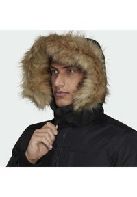 Černá parka s odnímatelnou kapucí, která má béžový kožich z umělé kožešiny. Texturovaná látka a přední zip. Model drží límec.